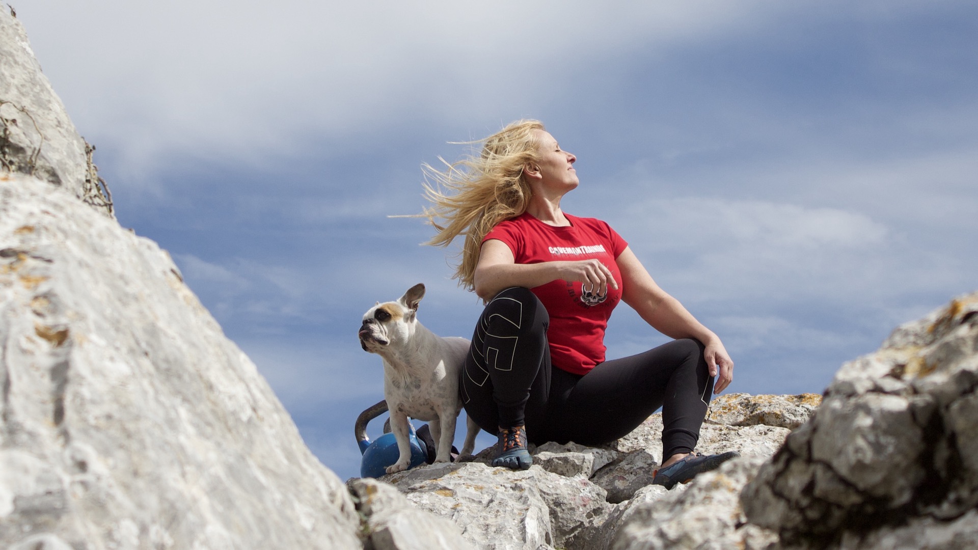 Anna sitting on mountain rocks with her dog, hair blowing in the wind
